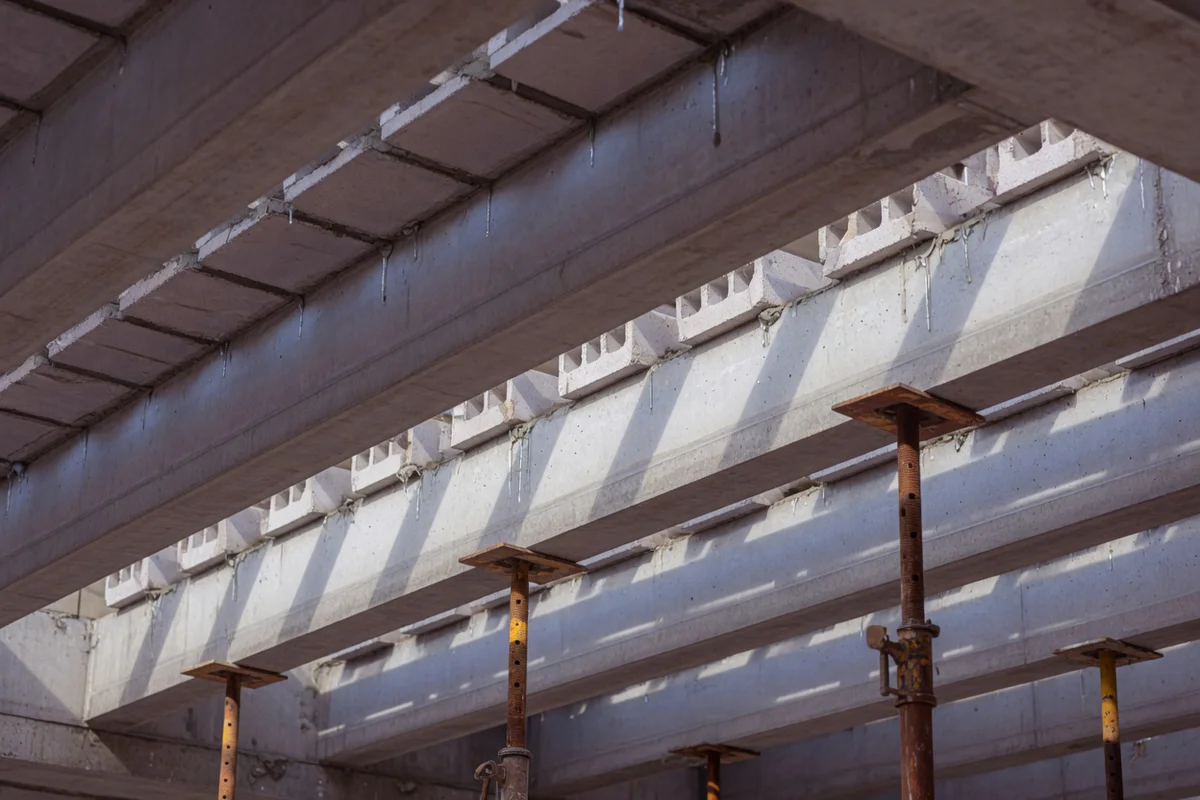 Underside view of a poutrelles-hourdis concrete floor slab supported by temporary steel shoring props during curing, illustra