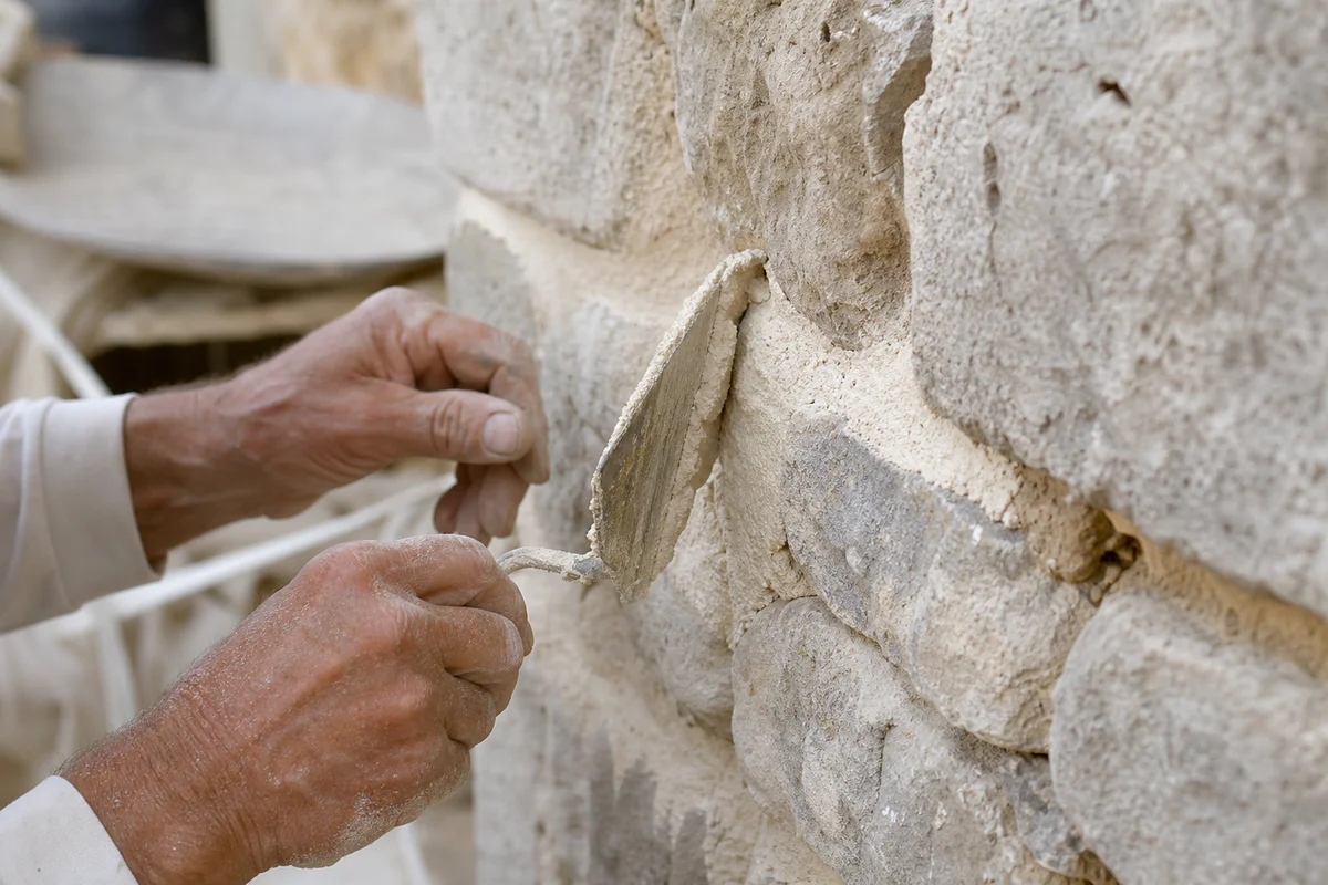 Artisan applying lime mortar to an old stone wall during traditional building restoration.