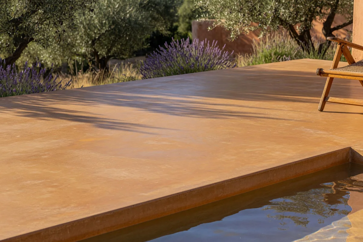 Coloration uniforme d'une terrasse en béton extérieur en ocre méditerranéen au soleil couchant, bordée de lavande et d'olivie